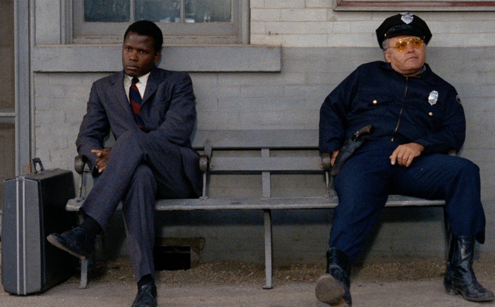 Actor Sidney Poitier and a cop sit on opposite sides of a bench, not looking at one another.
