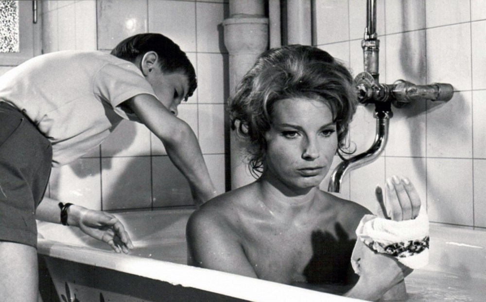 Actor  Gunnel Lindblom takes a bath; Jörgen Lindström stands outside the tub next to her.