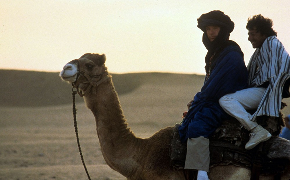 Actors Dustin Hoffman and Warren Beatty ride a camel in the desert.