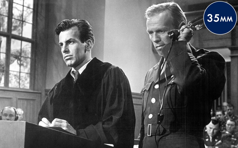 A man in a robe and another in a soldier's uniform stand next to each other in a courtroom.