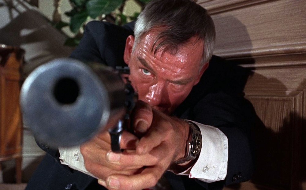 Actor Lee Marvin points a gun, his forehead covered in sweat.
