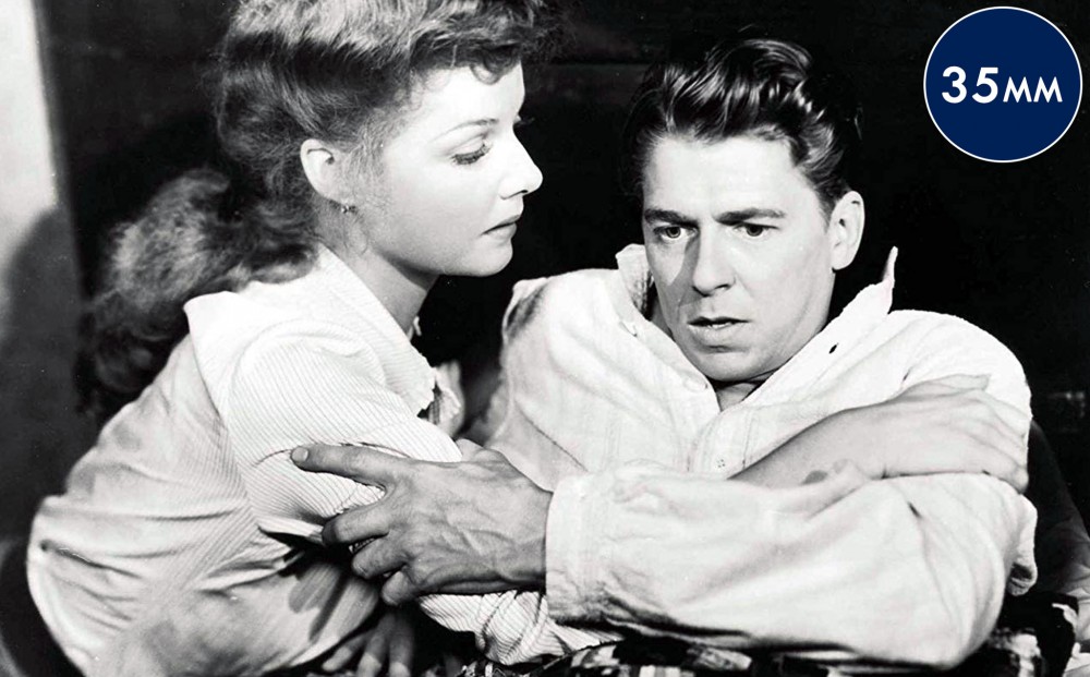 Actor Ronald Reagan grips the arms of actor Ann Sheridan, who kneels by his bedside.