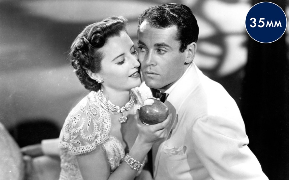 Actor Barbara Stanwyck holds an apple, her face right next to Henry Fonda's.