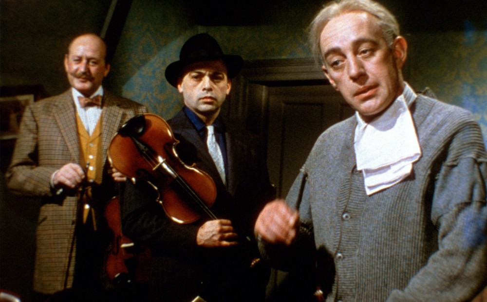 Three main characters all look in the same direction, standing in a parlor. The man in the middle holds a violin.