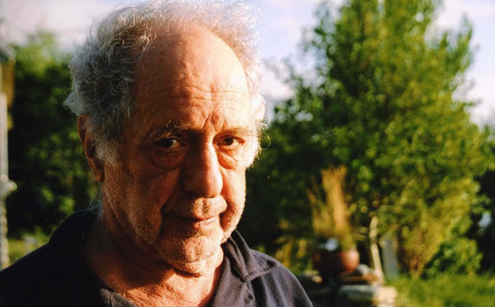 A close-up on Robert Frank, with a leafy green tree in the background.