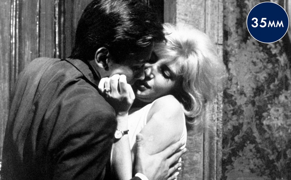 Actor Alain Delon presses his face to Monica Vitti's to kiss her.