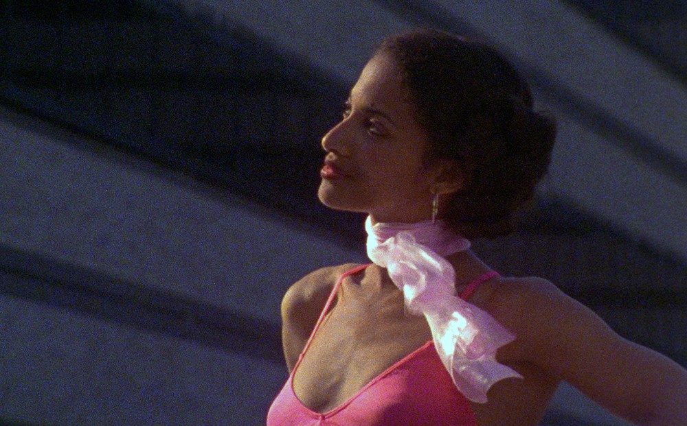 Actor Seret Scott looks off dreamily, wearing a pink spaghetti strap shirt and a pink scarf around her neck.