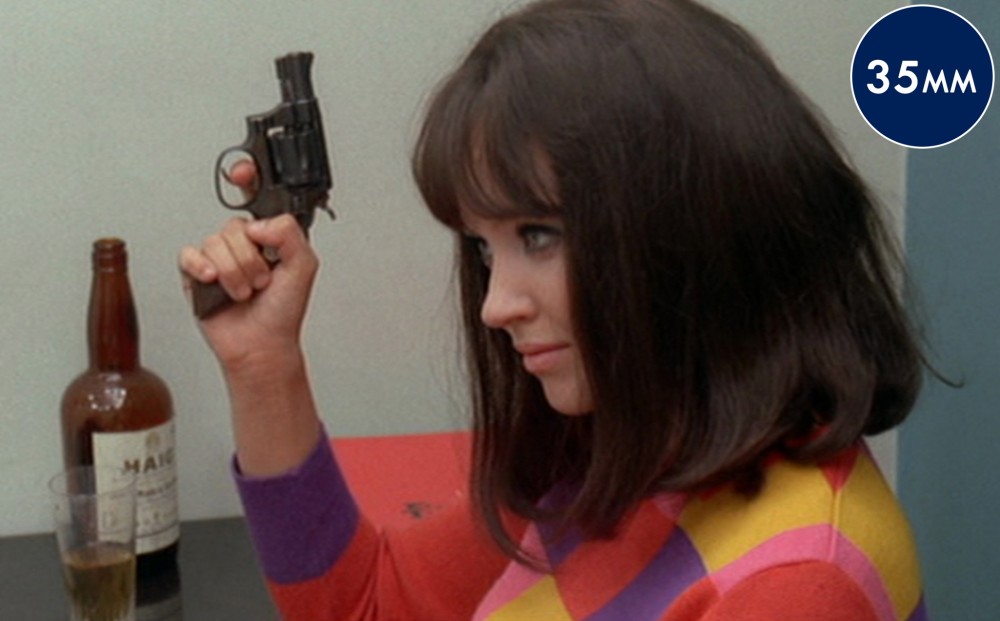 Actor Anna Karina holds up a small gun, he finger on the trigger.