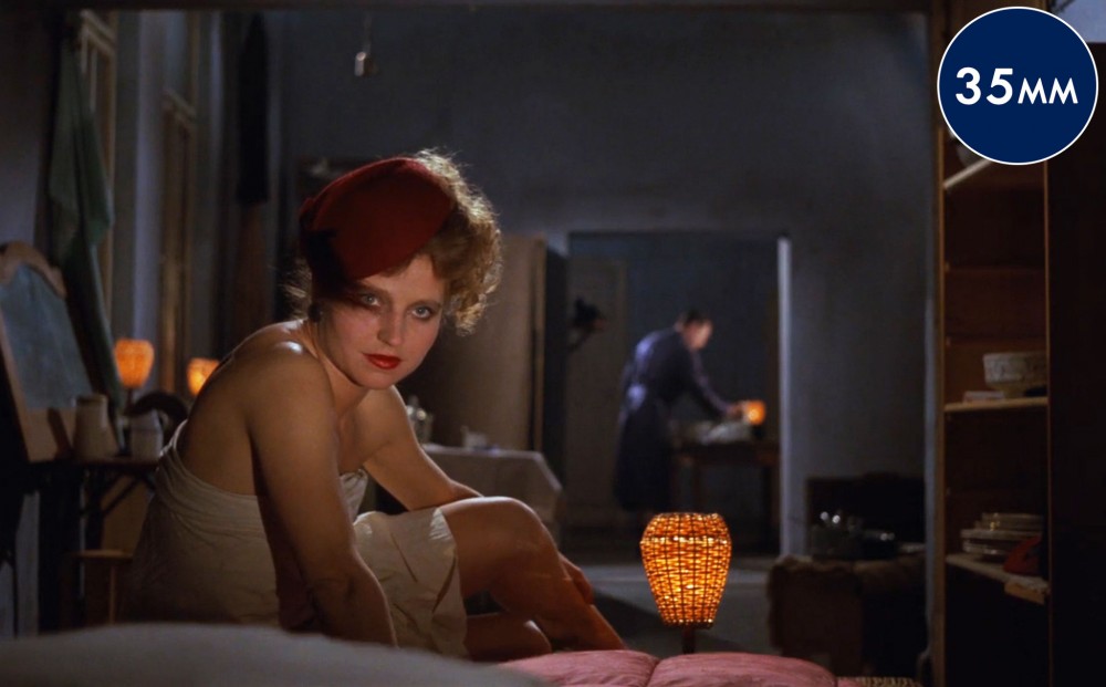 Actress Hanna Schygulla sits in a darkened room, lit by small orange lamps.