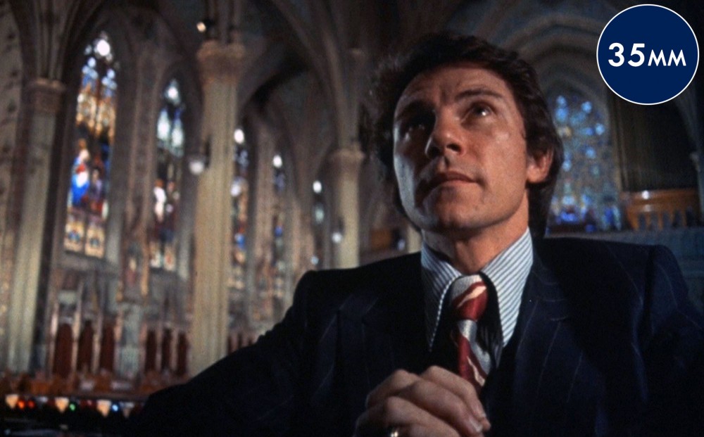 Actor Harvey Keitel sits in a church pew in a grand-looking cathedral, his hands clasped.