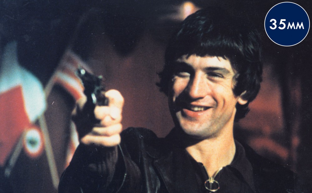 Actor Robert De Niro grins and points a gun.