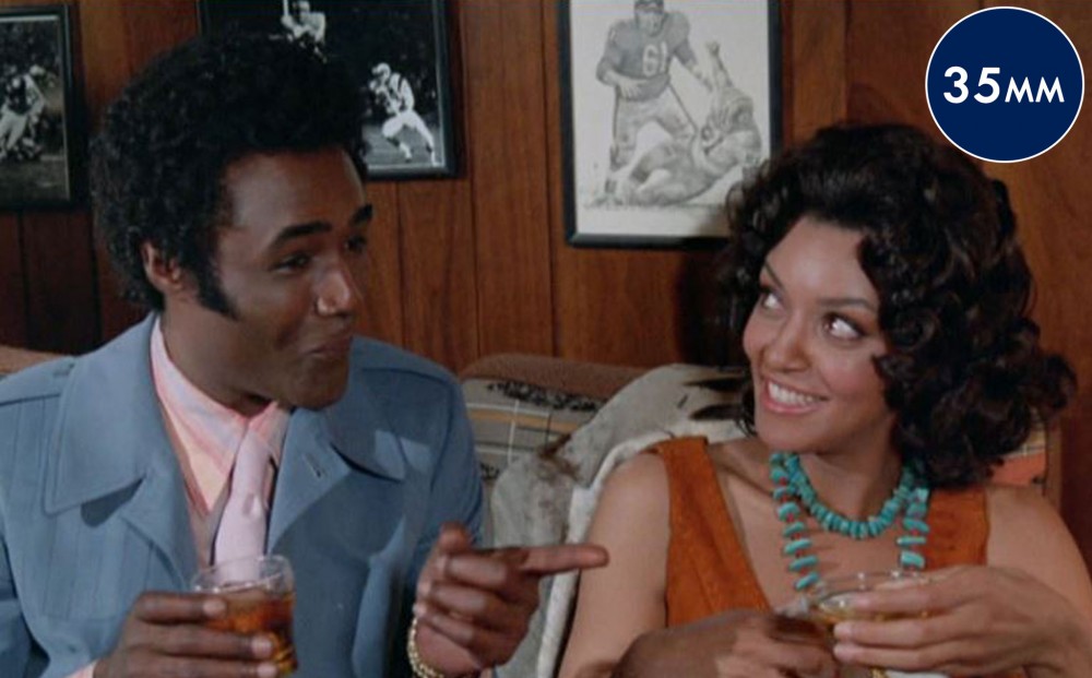 A man and woman sitting next to each other hold drinks and smile at one another.