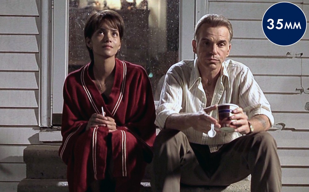 Sitting on the stairs of a small porch, Halle Berry wears a bathrobe and holds a cigarette, while Billy Bob Thornton sits next to her holding a pint of ice cream.