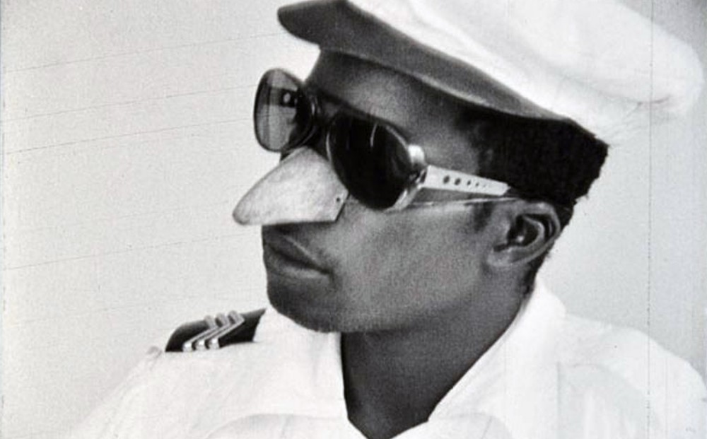 A man in a Navy officer's white uniform wears sunglasses and a fake nose.