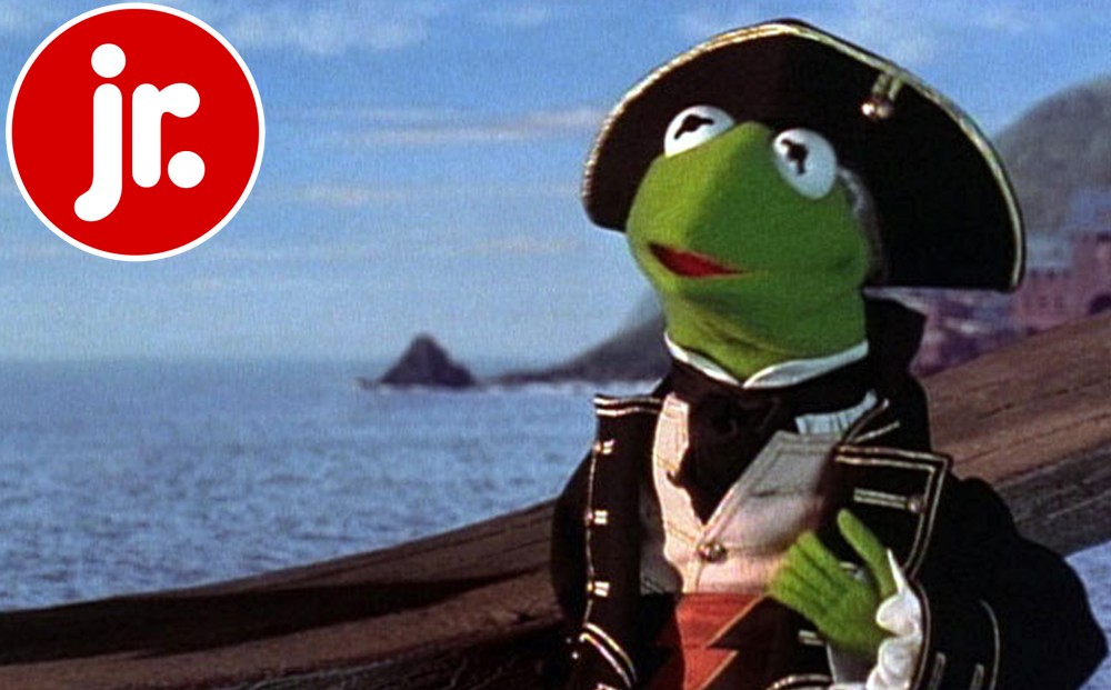 Kermit the Frog stands on the shore against a backdrop of ocean.