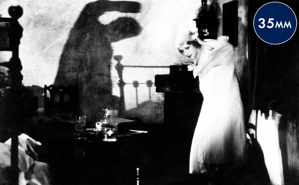 A woman leans away from a figure off-camera, whose shadow can be seen on the wall behind her.