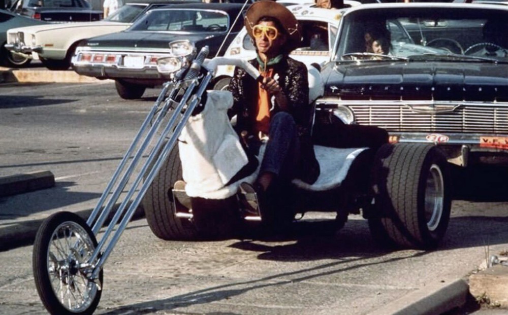 A man rides a three-wheeled motorcyle on a highway.
