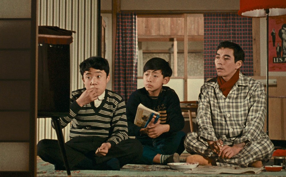 Two young boys and a man sit in front of a television.