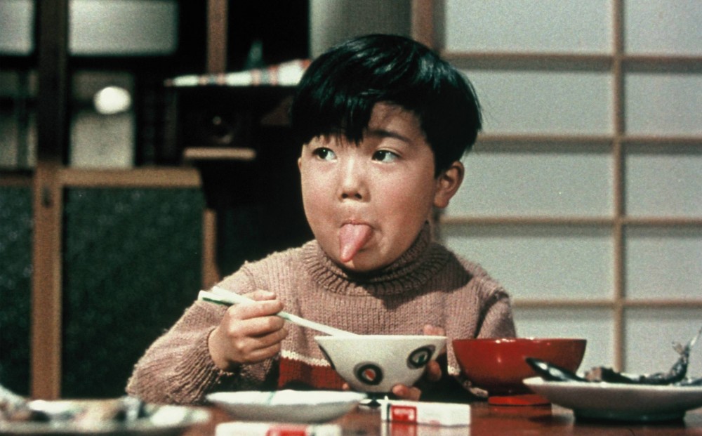 A young boy sits at a table and sticks out his tongue.
