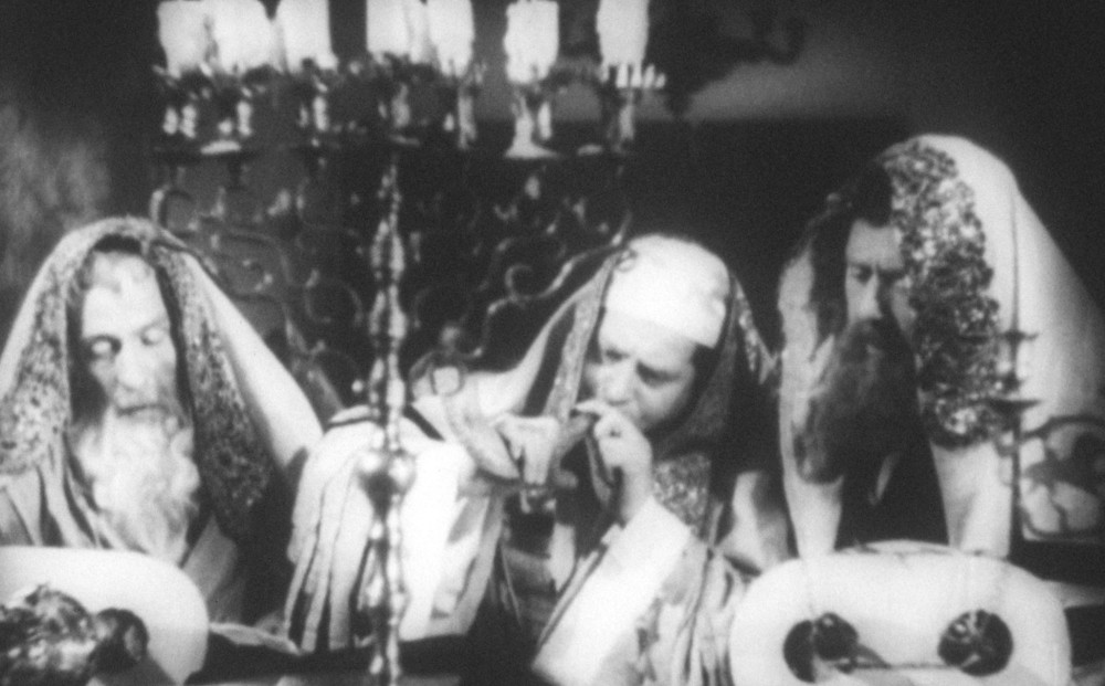 Three men wearing robes sit around a table with a large menorah.