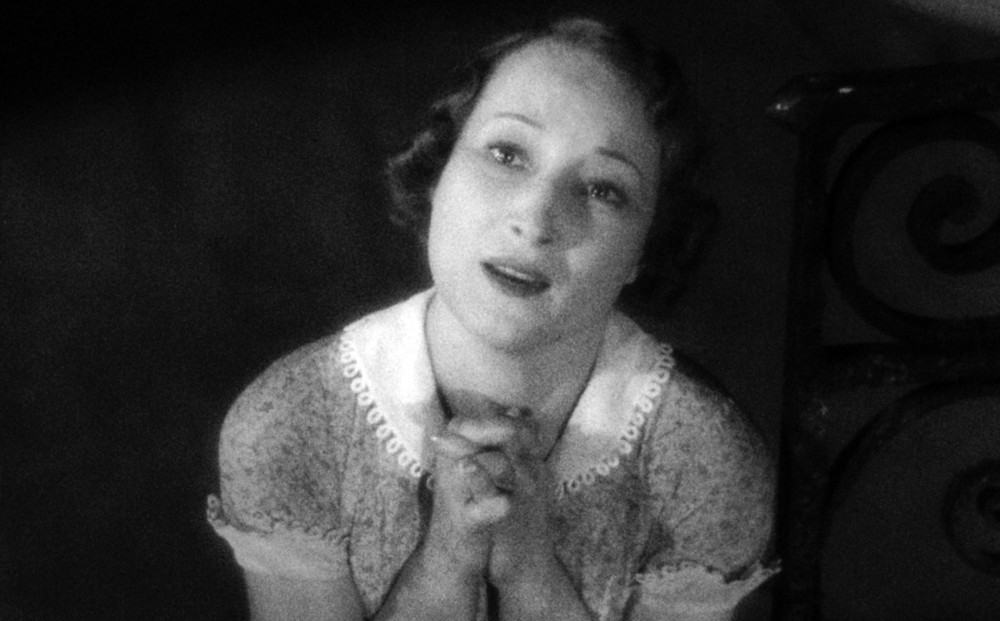 Actress Orane Demazis gazes up, with hands clasped to her chest, as though pleading.