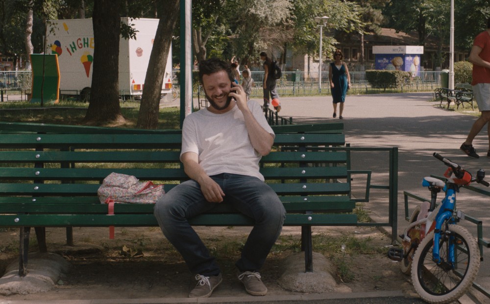 A man sits on a bench, smiling as he talks on a cell phone.