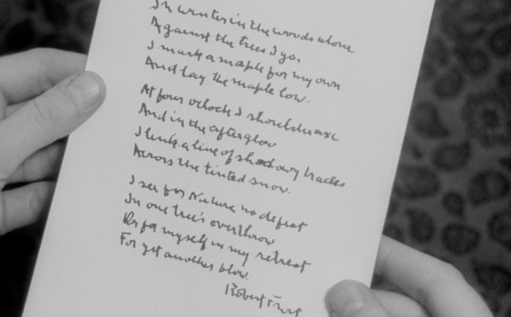 Two hands hold a sheet of paper with a poem by Robert Frost written on it.