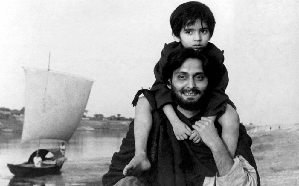 A young child sits on the shoulders of actor Soumitra Chatterjee, who is smiling.