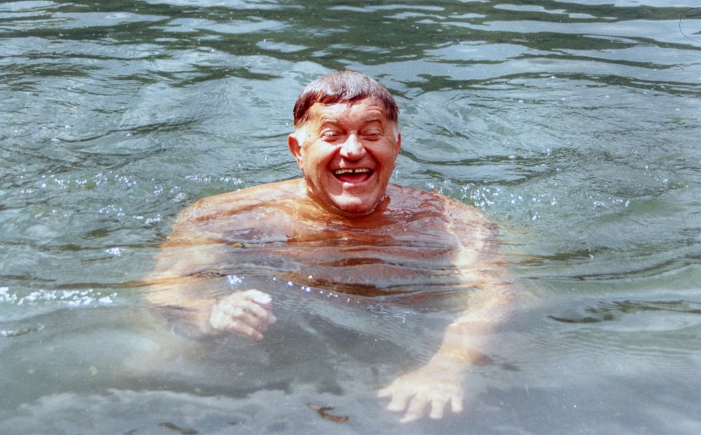 A man smiles while swimming, neck deep in water.