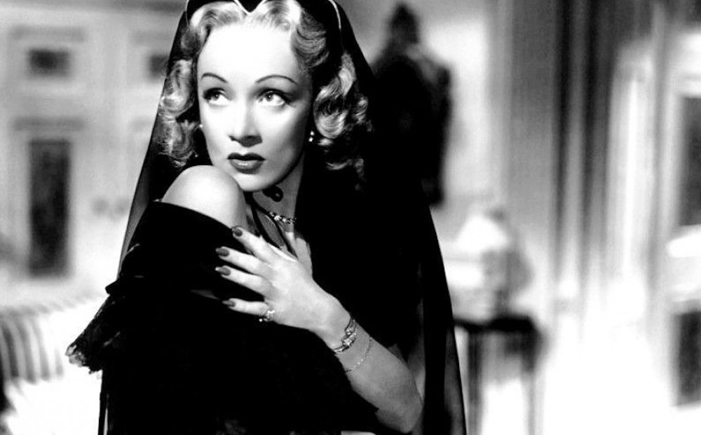 Actor Marlene Dietrich looks demure as she stares over her shoulder with one hand clutched to it.