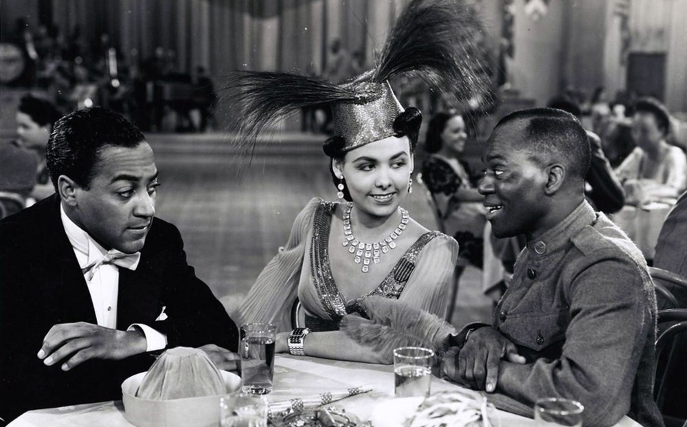 Lena Horne sits at a table in a nightclub with two men.