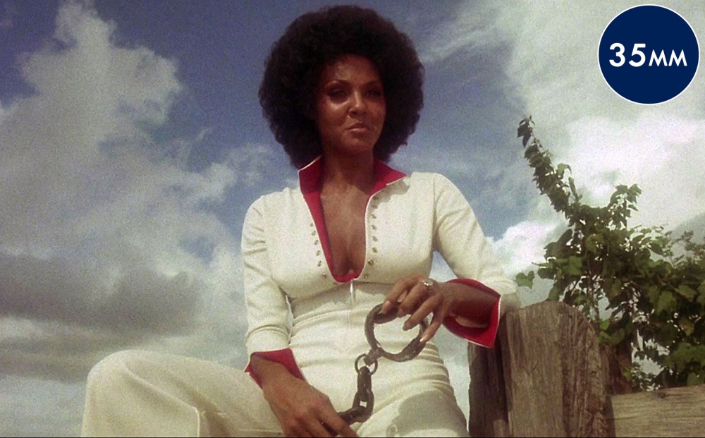 Actor Marki Bey wears a white jumpsuit with red accents, and holds handcuffs.