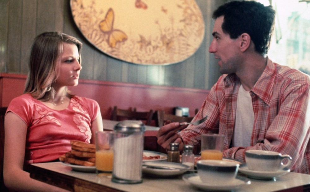 Actors Jodie Foster and Robert De Niro eat breakfast at a diner table.