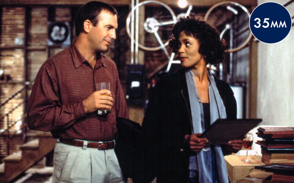 Whitney Houston and Dennis Quaid smile at each other.