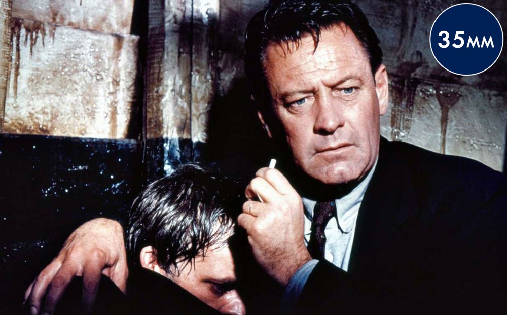 Actor William Holden has his arm around another actor whose face is partially obscured.