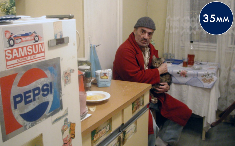 A man sits in his kitchen, holding his cat in his lap.
