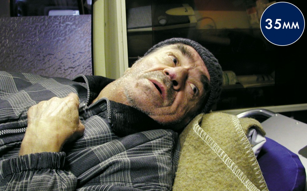 Close-up on a man's shoulders and face, laying down on what appears to be a stretcher.