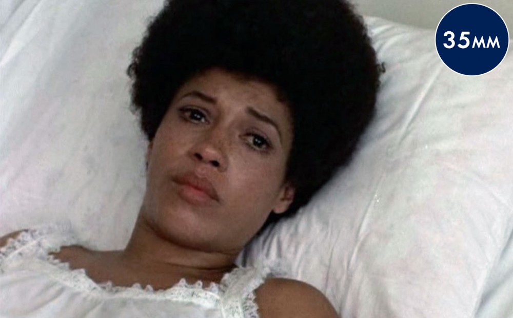 Actor Diana Sands reclines on a pillow, wearing a white nightgown; she has tears in her eyes.