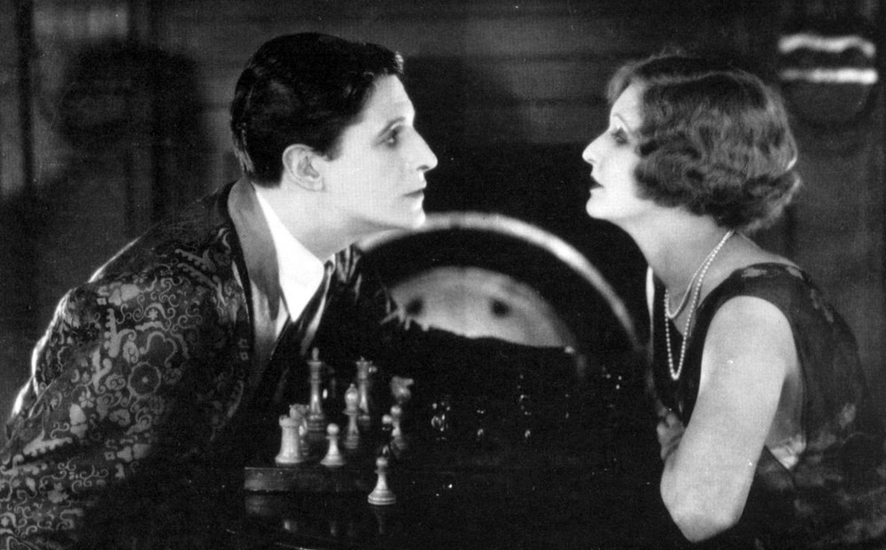 A man and woman sit across from each other with a chess board in between them.