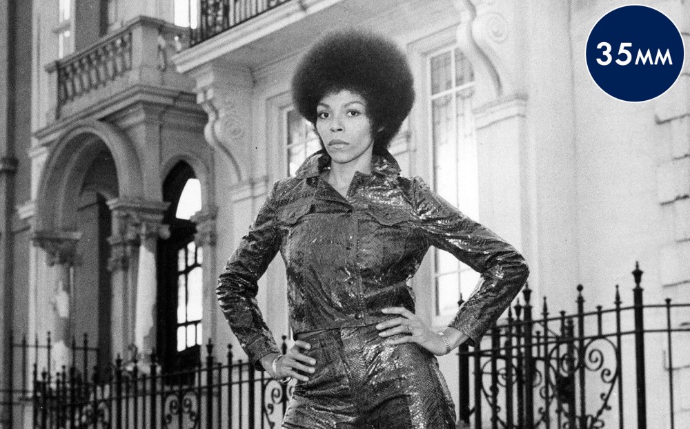 Actor Rosalind Cash stands with her hands on her hips, wearing matching leather pants and jacket.