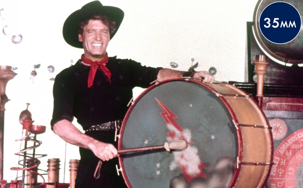 Actor Burt Lancaster grins while holding a huge drum.