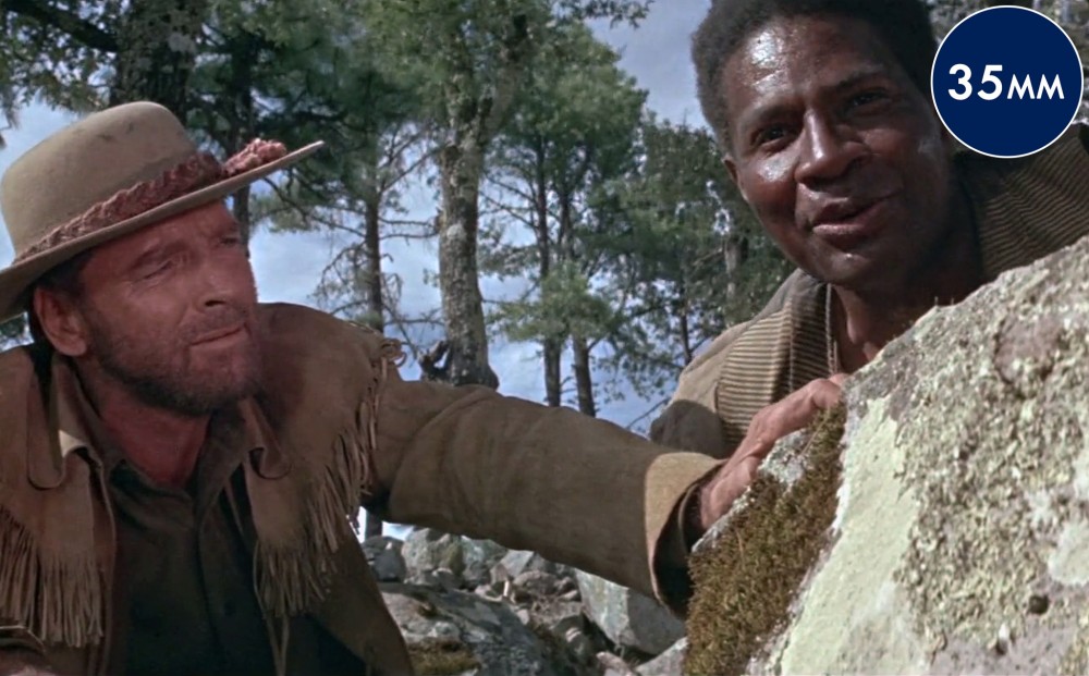 Actors Burt Lancaster and Ossie Davis look out from behind a crop of boulders.