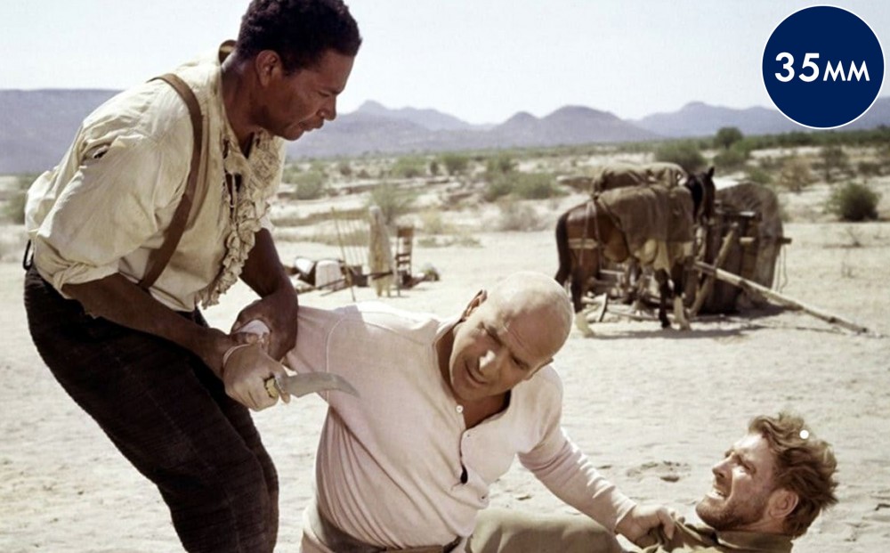 Actor Burt Lancaster is held to the ground by Telly Savalas, who holds Lancaster's collar in one hand and a knife in the other. Ossie Davis holds him back, grasping the arm with which Savalas hold the knife.