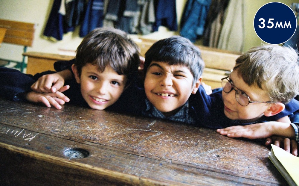 Three young boys sit at a classroom desk.