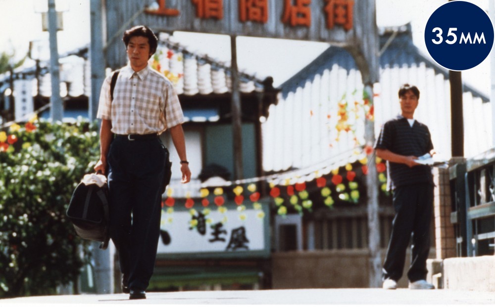 A man walks down a Tokyo street holding a duffel bag.