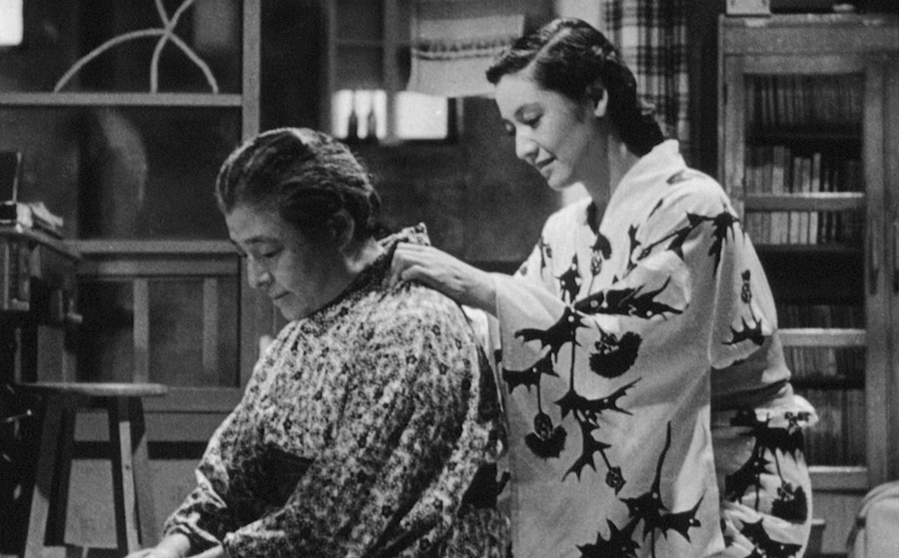 One woman helps another get dressed in her kimono.