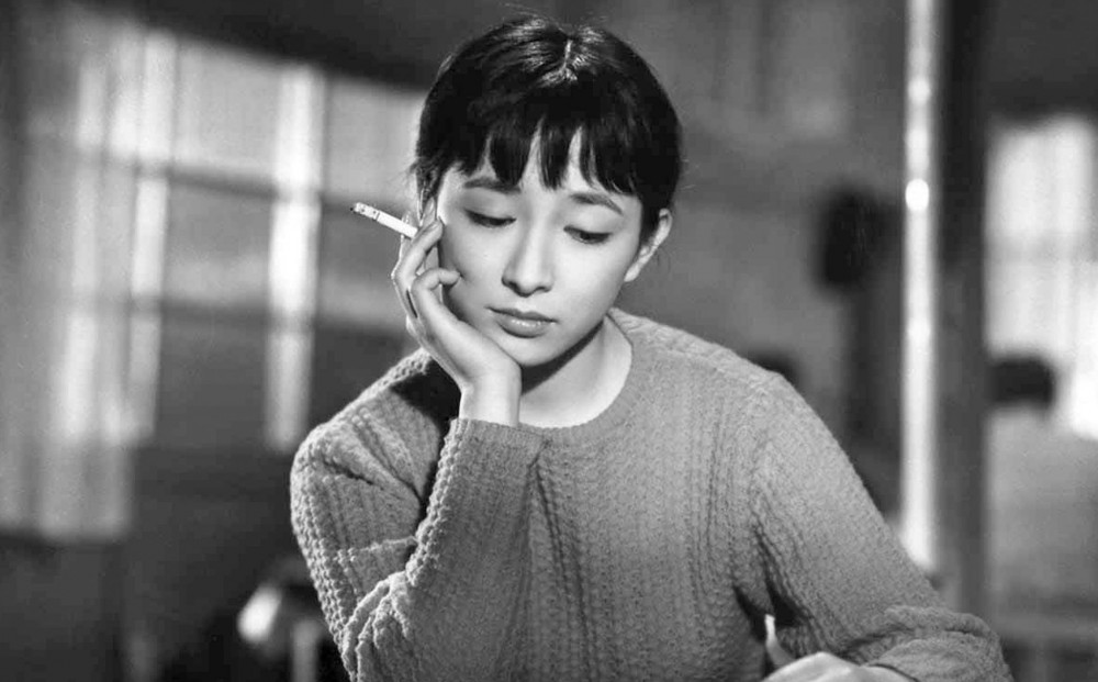 Actor Ineko Arima sits at a table, her head rested on a hand holding a cigarette.