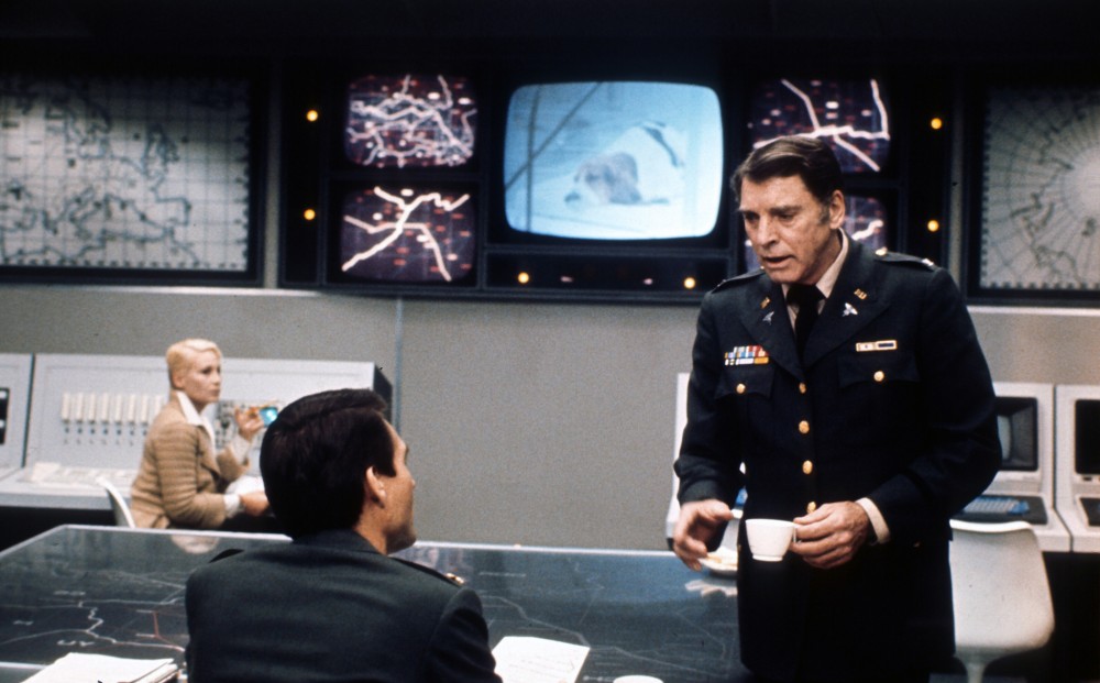 Two men converse in a military command center.