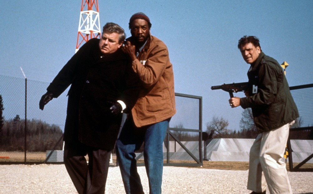 One man holds another by the collar, while Burt Lancaster stands nearby holding a gun.