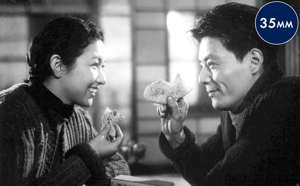 A man and woman face each other, eating and smiling.